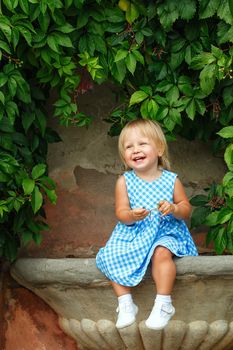 Little blonde girl on a background of green grape leaves