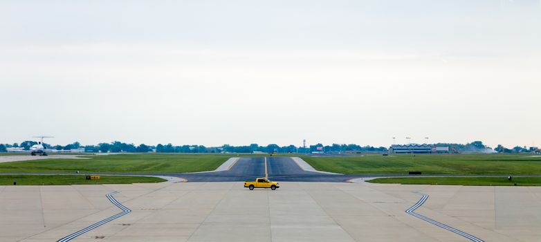 A yellow servicing truck moving on the middle of airport runway