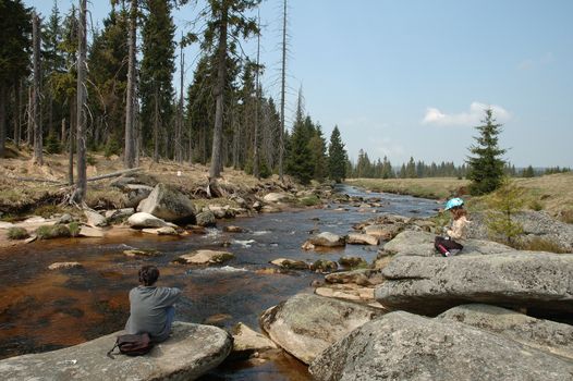 Mother and daughter resting on rocks on river bank in izerskie mountains in Poland