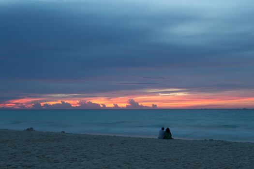 Couple sitting on the sandy beach looking at Cozumel Island at sunrise in Mexico