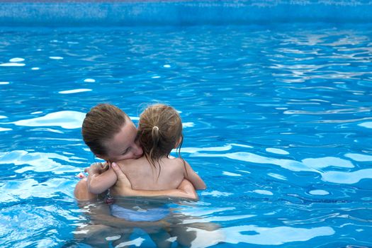 Mother and daughter cuddling in the pool with copy space on the right