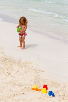 Cute toddler playing by the beach with her colorful sand toys