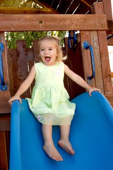 Two years old girl fulfilled on the blue slide that attached to the wooden playground