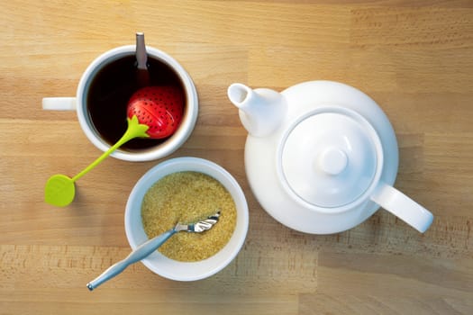 Infused tea, teapot  and brown sugar next to each other on beech wood, shot from top