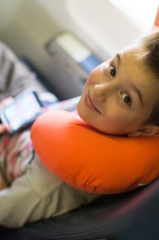 Kid travelling with his player and orange neck pillow on the airplane