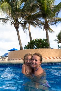 Mother and daughter having great time in the swimming pool under the palm trees