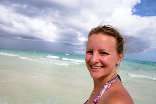 Woman at the beach smiling naturally, green sea at the background.