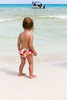 Little girl in her bikini bottom observing the boat on the sea