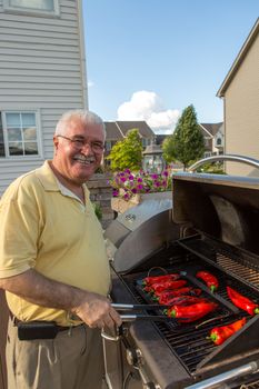 An Old Man wearing a yellow shirt is happily grilling chilies
