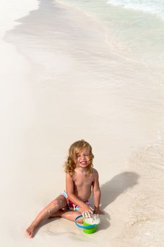 Little girl playing with the sand by the beach happily smiling
