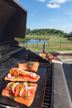 Fresh filleted salmon steaks on the barbecue topped with seasoning in the form of onion, tomato and herbs during preparation and grilling of a delicious seafood meal