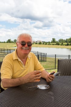 Senior Man posing with his smart phone  while drinking his Turkish tea at the patio by the pond