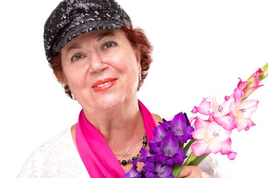 Senior lady smiling to camera happily with her black stylish hat and holding gladiolus flowers. Isolated on white.