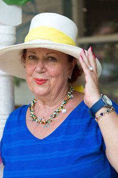 Beautiful chic senior woman in a wide-brimmed straw sunhat and fashionable jewellery looking at the camera with a lovely smile