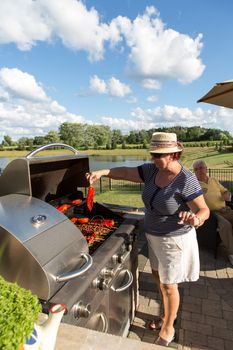 An old couple enjoying grilling barbecue near a lake.