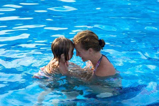 Mother and doughter head to head having passionate great time in the swimming pool.