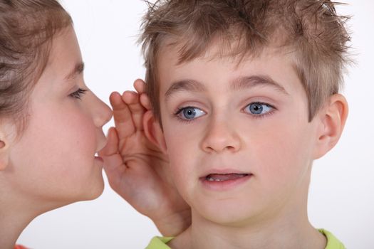 Young girl whispering into a boy's ear