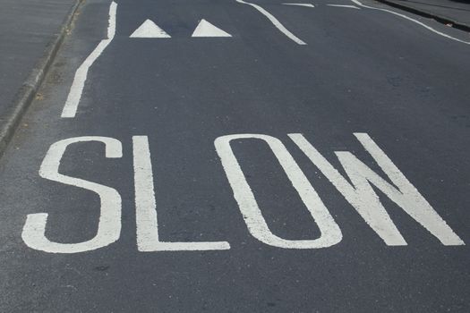 painted road warning saying 'slow' and speed bumps