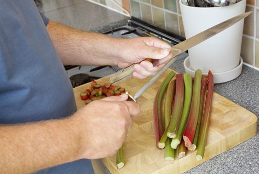 Male cook sharpening knife on a steel in a domestic kitchen. There is rhubarb on the chopping board.