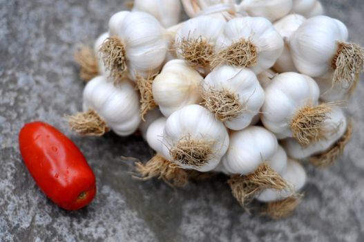 Garlic bulbs braid and one tomato on a gray raw stone table
