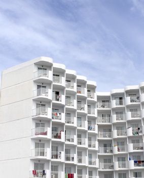 Tall white tourist hotel with cloudscape background.