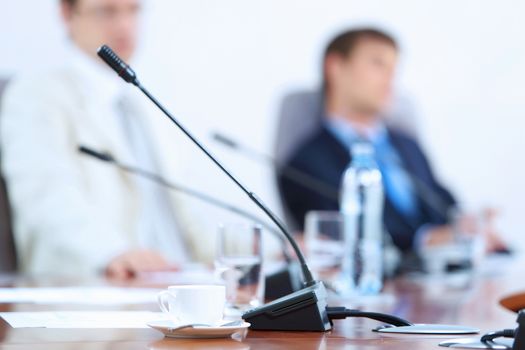 Image of microphone standing on table at conference against defocused background of two businessmen