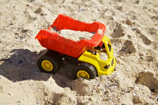 Child Playing With Yellow and red Plastic Truck in Sand