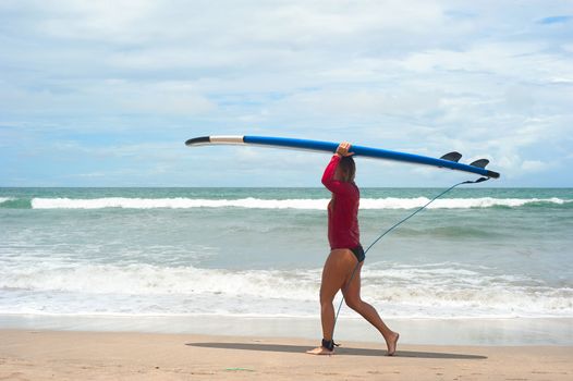 Bali island, Indonesia - March 09, 2013: Unidentified woman walking with a surfboards on the beach  in Bali island, Indonesia. Bali is one of the top of world surfing destinations.