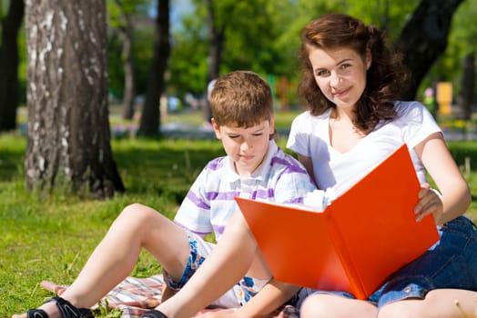boy and a woman in a summer park reading a book together