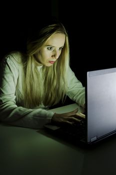 woman working on a computer by night in a dark room with only light from computer falling on her face vertically cropped