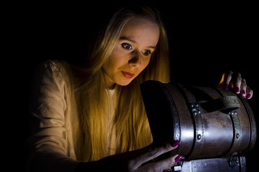 woman secretly opening a small chest in the dark with lights coming from it and falling on her face