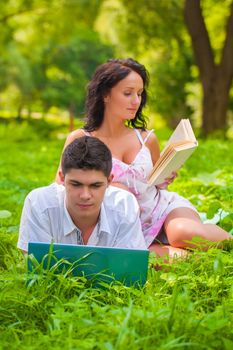 couple lying with laptop and book at park