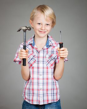 A cute smiling boy holding a hammer and a screwdriver