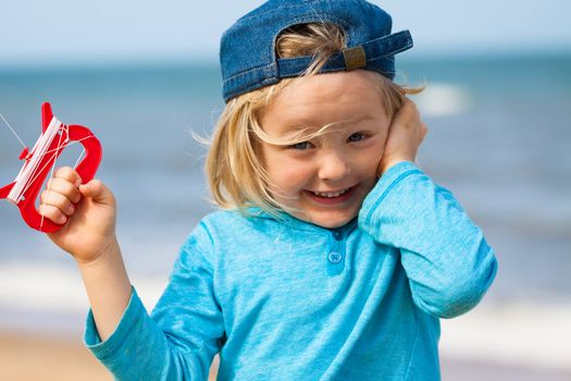 A happy excited and cute young boy flying a kite at the beach.