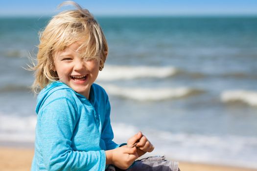Portrait of a very cute happy boy laughing at camera at the beach.