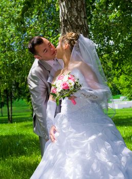 The wedding pair kisses near a tree trunk