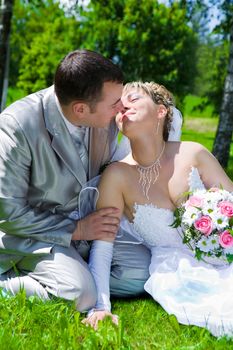 The wedding pair sits on a grass kiss