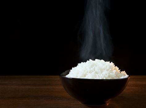 white steam rice in black ceramic bowl with smoke on black use for food topic