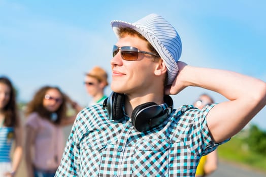 young man in sunglasses, a hat holds a hand on a background of blue sky and friends