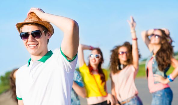 young man in sunglasses, a hat holds a hand on a background of blue sky and friends