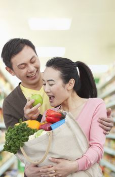 Man Feeding Woman Apple in Grocery Store