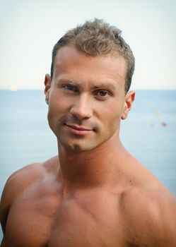 Portrait of handsome young muscle man smiling, outdoors, showing muscular pecs