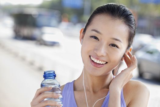 Young Woman with Bottled Water Listening to Music