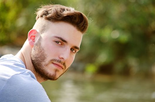 Portrait of handsome young man outdoors in nature, looking in camera