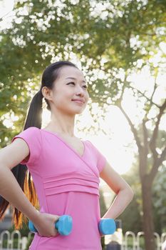 Young Woman Exercising in Park with Dumbells