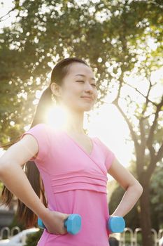 Young Woman Exercising in Park with Dumbells