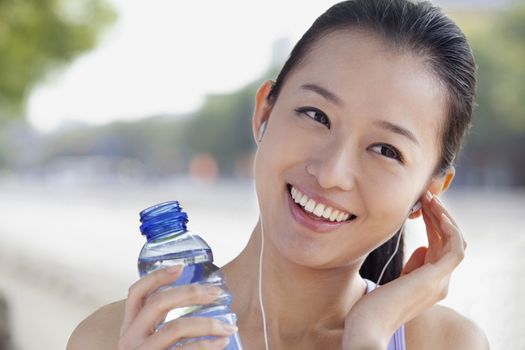 Young Woman with Bottled Water Listening to Music