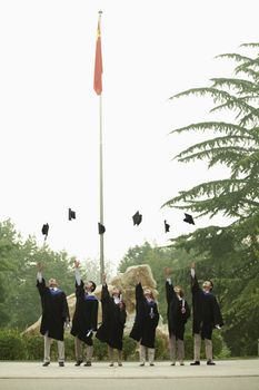 Young Group of University Graduates Throwing Mortarboards in the Air, Vertical