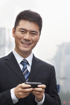 Young Businessman Smiling and Using a Smart Phone, Looking at Camera