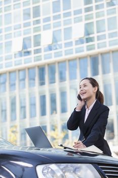 Businesswoman Standing by Car Using Phone and Laptop